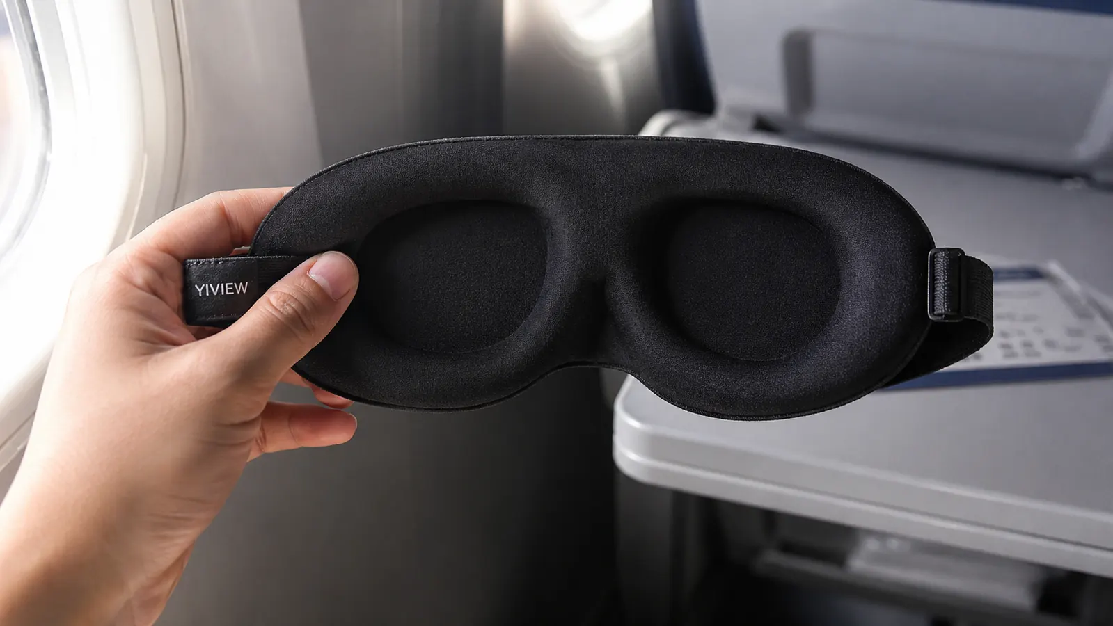 Close-up of a hand holding the YIVIEW 3D contoured sleep mask, showing the molded eye cups from the inside