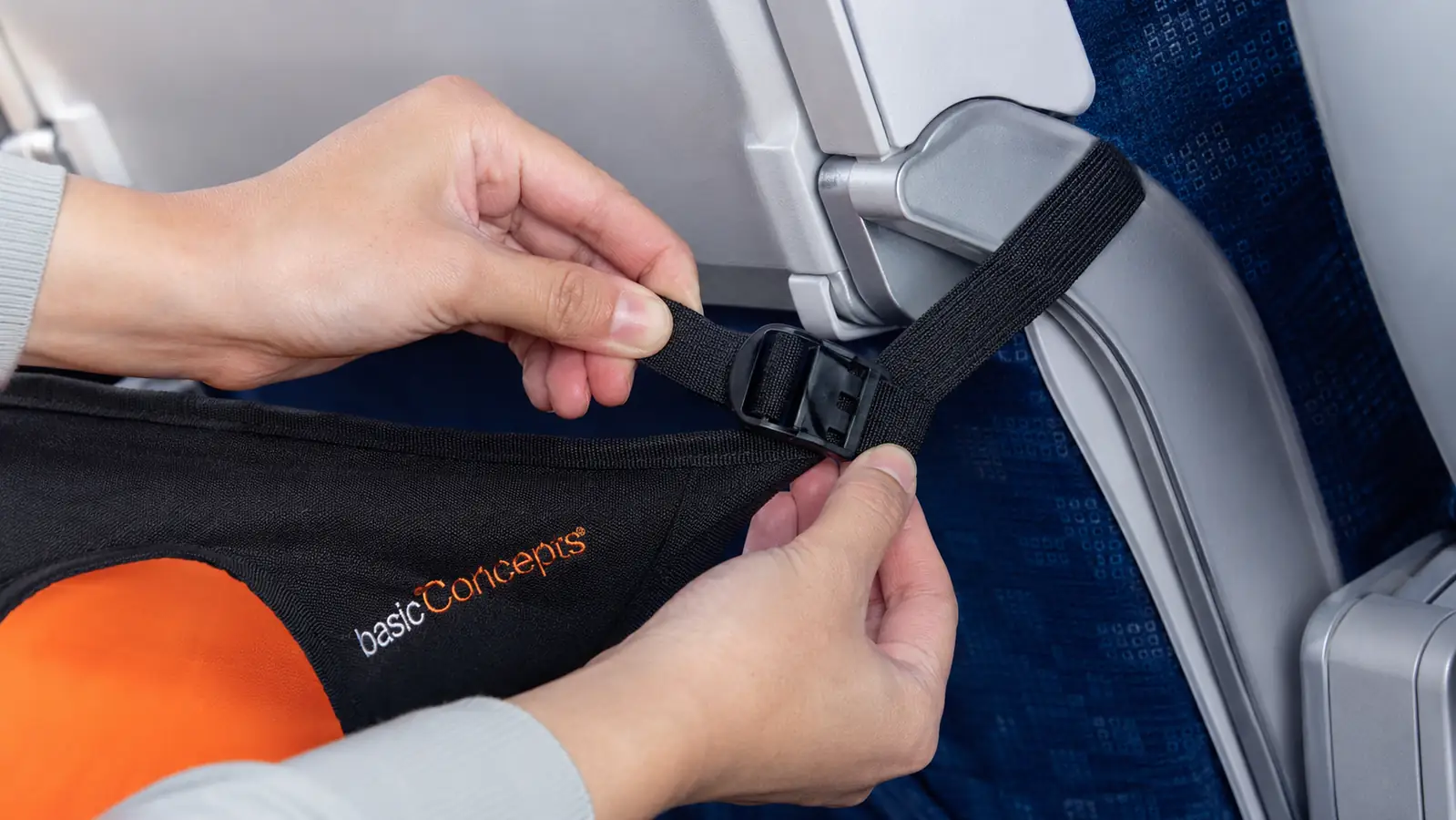Hands adjusting the straps of the BASIC CONCEPTS foot hammock around a tray table arm