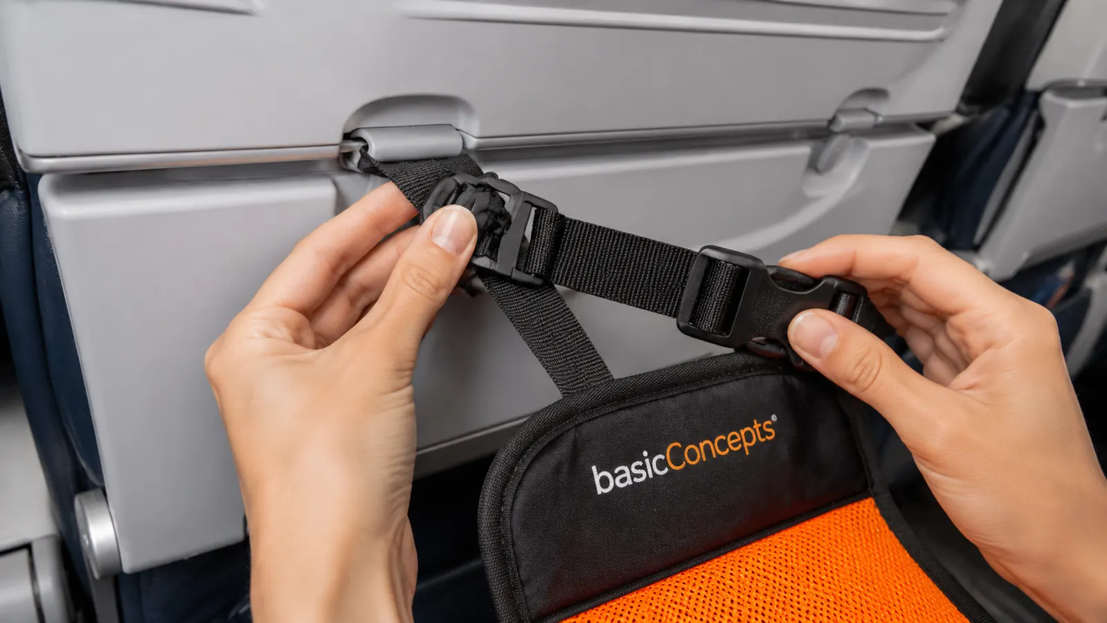 Hands adjusting the strap and buckle of the BASIC CONCEPTS foot hammock around a tray table arm