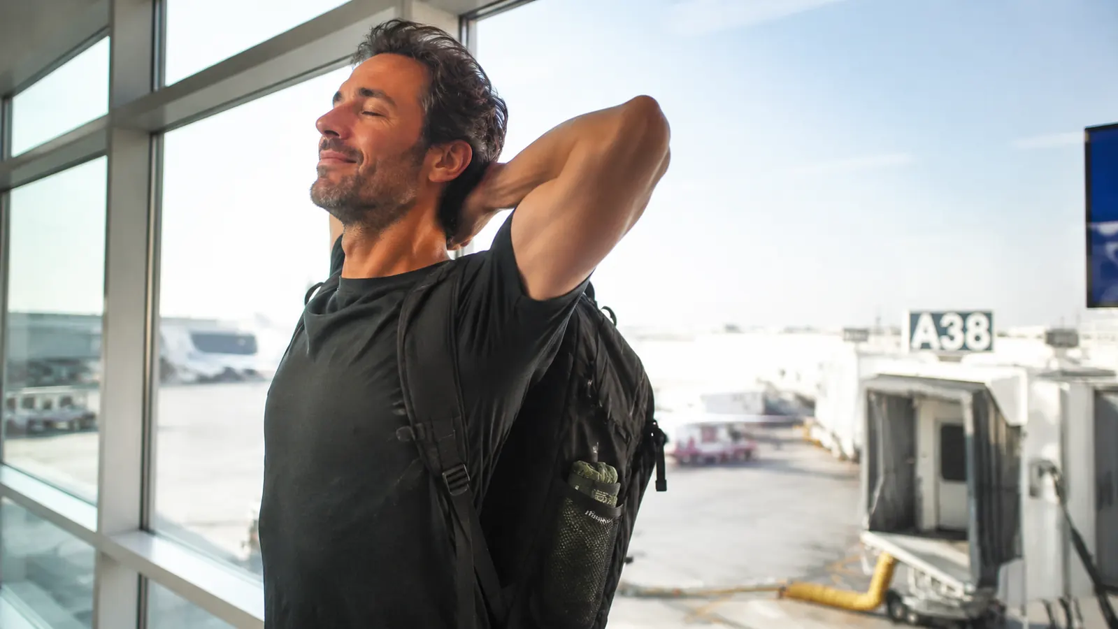 Traveler stretching her legs in an airport terminal after a long flight, foot hammock visible in an open backpack pocket